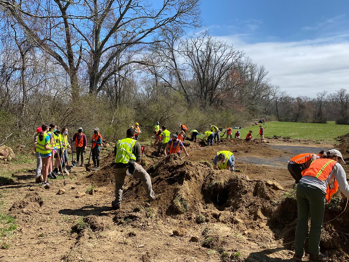 Volunteers in safety vests digging and restoring land as part of South Kingstown Land Trust's conservation efforts.